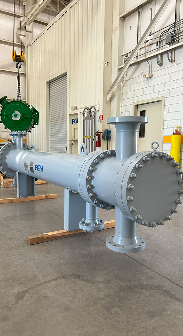 An industrial heat exchanger in a workshop, featuring a cylindrical shell, bolted flanges, and support stands.